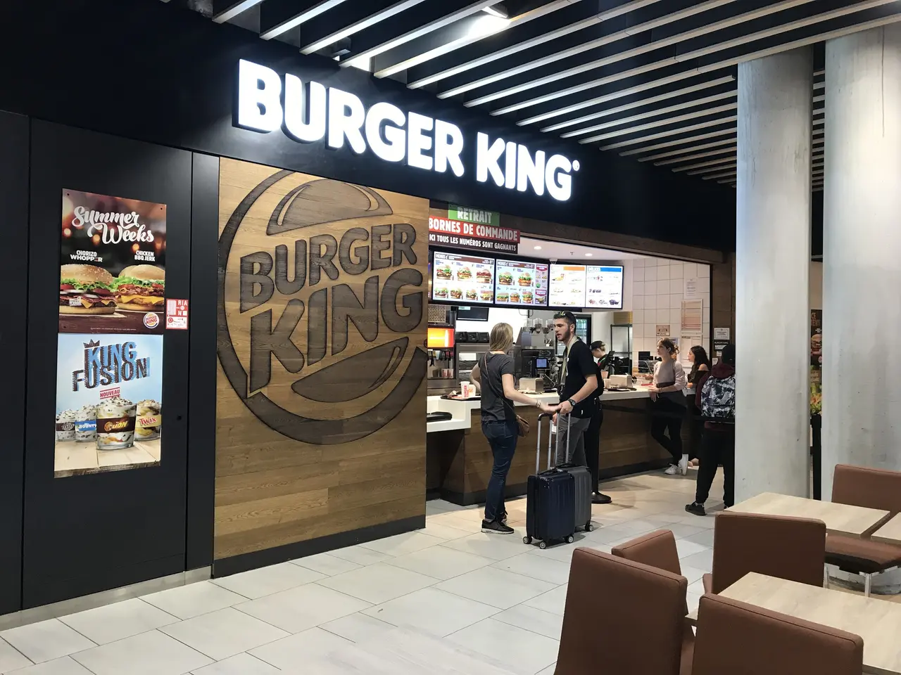 L'immagine mostra un ristorante Burger King all'aeroporto, con un gruppo di persone in piedi sul...