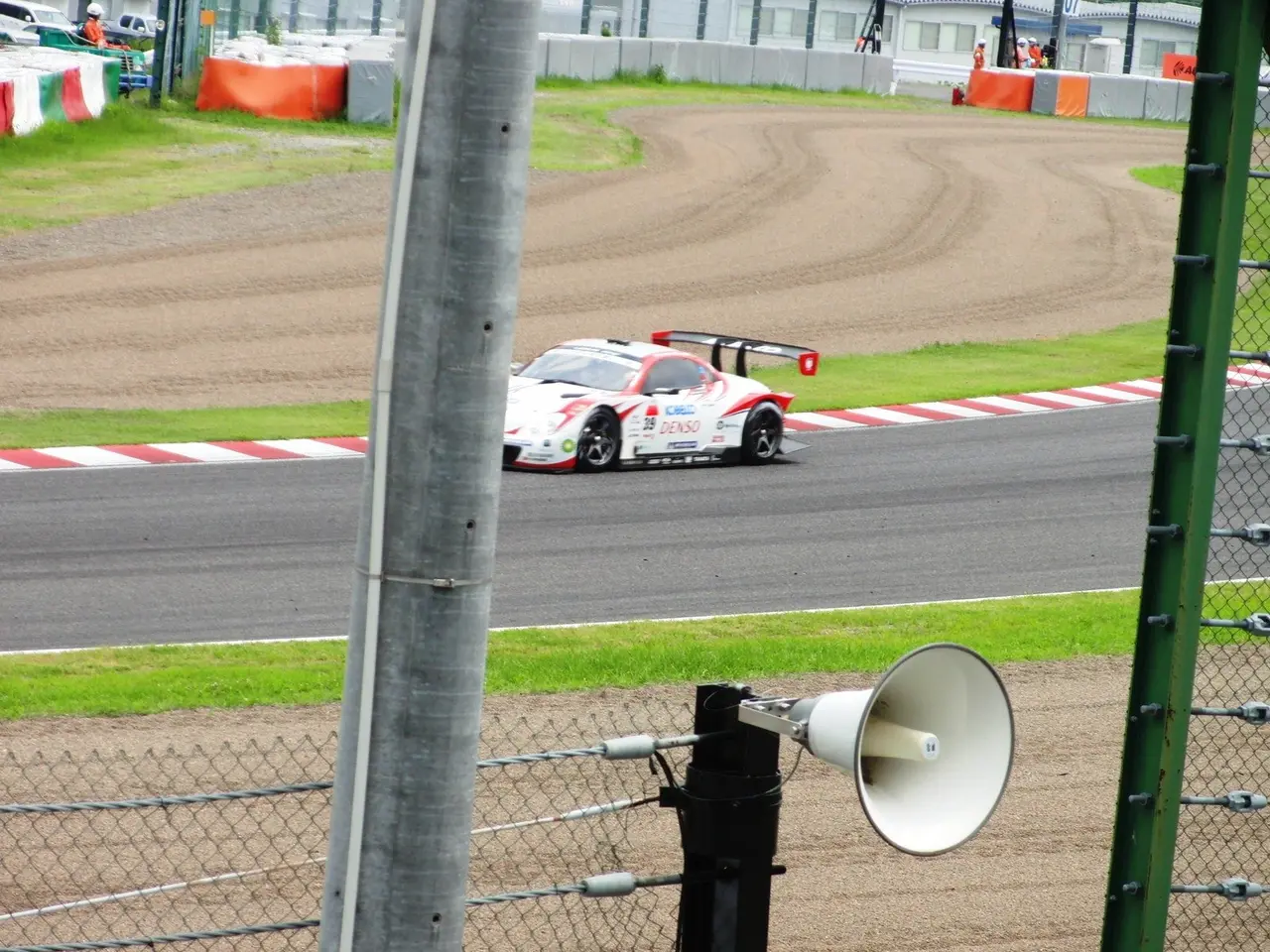 L'immagine mostra un'auto da corsa che corre su una pista con un megafono davanti. La pista è...