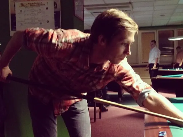 L'uomo con la camicia a scacchi rossa e i pantaloni neri sta giocando a una partita di snooker....