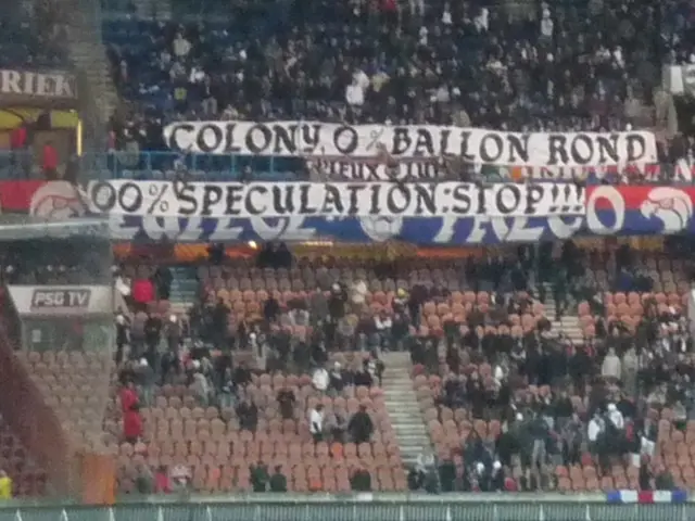 Questa immagine è stata scattata in uno stadio. In primo piano, si vede una grande folla e bandiere...