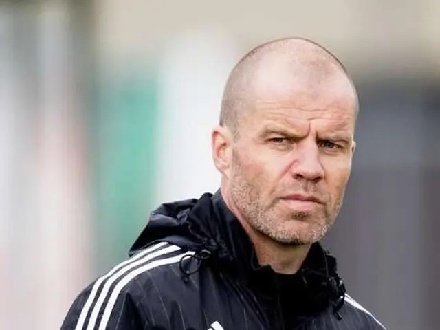 L'immagine mostra un uomo calvo in giacca nera in piedi su un campo da calcio, con uno sfondo...