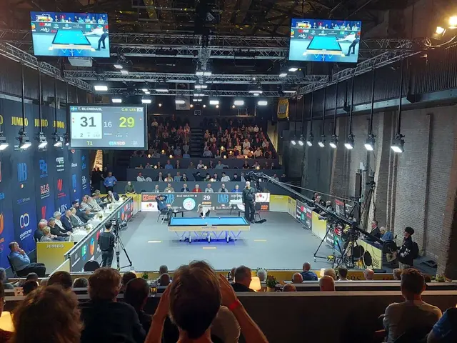 L'immagine mostra una grande folla di persone sedute di fronte a un palcoscenico, con un tavolo da...