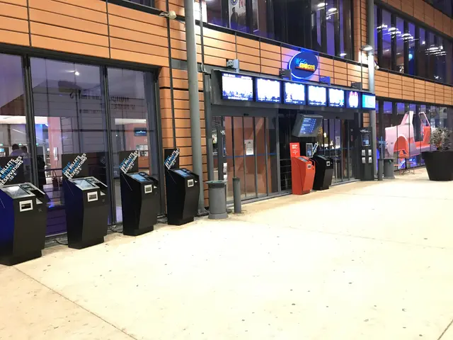 L'immagine mostra una stanza ampia piena di molte televisioni a parete, finestre di vetro, luci e...