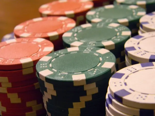 L'immagine mostra una pila di fiches da poker di diversi colori posizionate su un tavolo di legno....