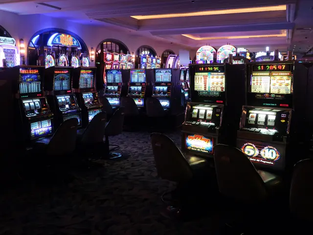 L'immagine mostra una fila di macchinette per il casinò con sedie sul pavimento e luci sul...